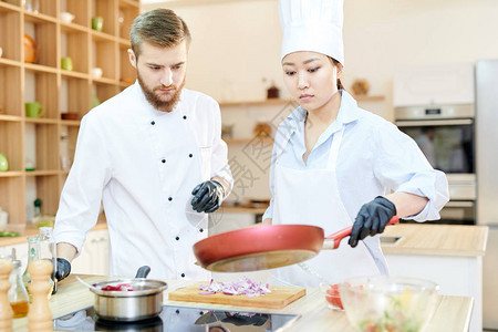 亚洲女厨师在现代餐厅厨房和复印空间的炉灶上架着煎锅的亚图片