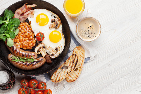 英语早餐炒鸡蛋香肠培根豆类吐司西红柿橙汁和木制图片