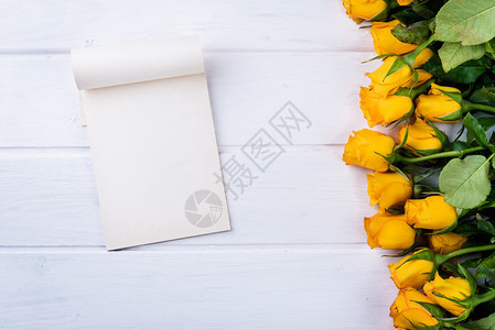 白色木桌上的黄玫瑰和纸图片