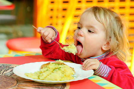 小孩子在小桌子后面吃土豆泥背景图片