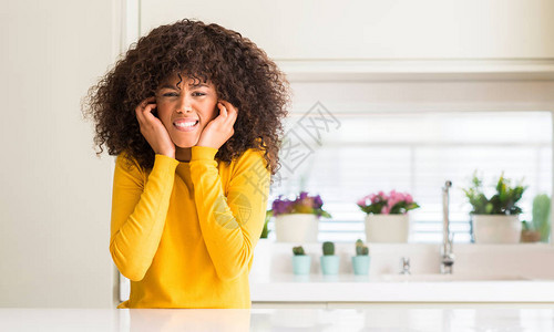 衣着黄色毛衣的非洲女在厨房用指头遮住耳朵图片