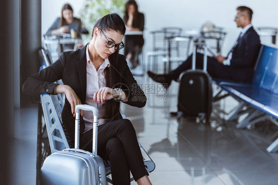 成年女商人在机场看望手表和等待离境图片