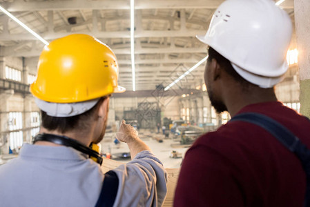 戴着安全帽和工作服的留着胡子的工程师站在现代工厂宽敞的生产部门图片
