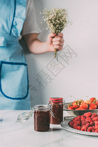 围裙上的妇女在桌边拿着鲜花草莓草莓和果酱罐头的花图片