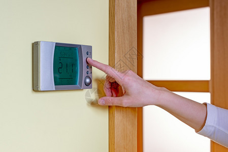妇女用手在现代可编程的自动调温器上安装房间温度图片