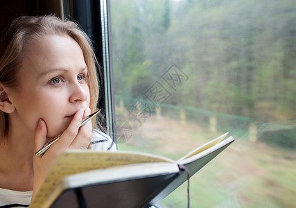 火车上的年轻女子在日记或日记上写笔记图片