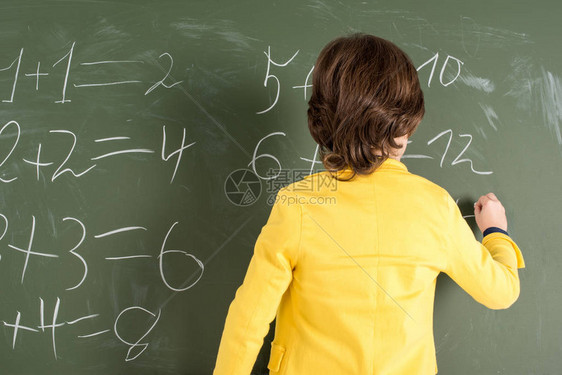 小学生用粉笔在黑板上写字的背影图片