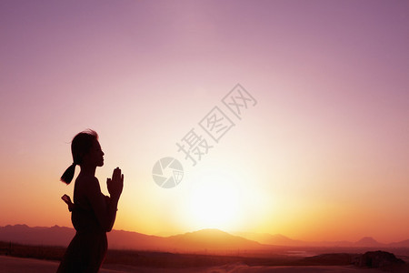 带着双手祈祷的贞洁年轻女子在沙漠露出姿势轮光图片