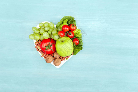 以蓝色健康饮食概念隔离的心形盘子上新鲜有机蔬菜和水图片