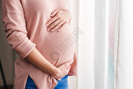 怀孕妇女站在家窗户旁边时摸肚子时图片