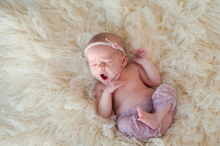 一个打呵欠的10天大的新生女婴的画像她蜷缩着睡在奶油色的弗图片
