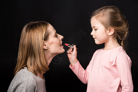 可爱小女儿的侧面观对母亲涂口红用图片