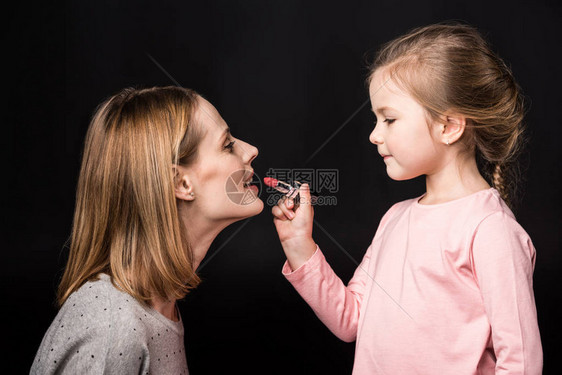 可爱小女儿的侧面观对母亲涂口红用图片