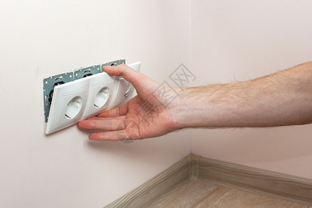 安装墙壁电源插座的电工的手图片