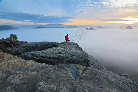 徒步旅行者在山谷上方的岩石尽头男人看着朦胧和秋天的早晨山谷到明亮的早晨太阳游客正在寻找迷雾笼罩的山谷秋图片