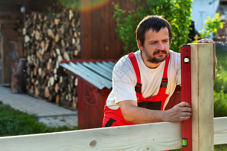 男子在后院建造木栅栏用水平仪检查柱图片