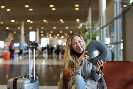 女孩坐在机场候机室坐着颈枕和行李图片