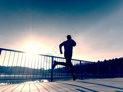 晨跑者穿着高大的黑色紧身裤在桥上锻炼在湖桥上光滑的混凝土地面上进行户外锻炼太阳勾图片