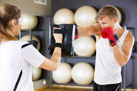 健身俱乐部教练持有的年轻男拳击手出气筒两个年轻而专注的人成对训练拳击作为在健身背景图片