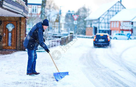 有雪铲的人在降雪期间在冬天清理人行道欧洲的冬天穿着温暖冬衣的年轻人德国的雪和天气混乱暴风雪和大背景图片