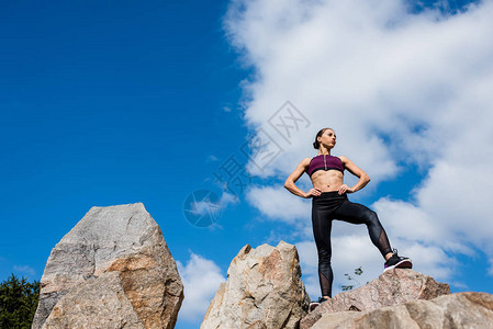 双臂叉腰站在岩石上的健康女人的底视图图片