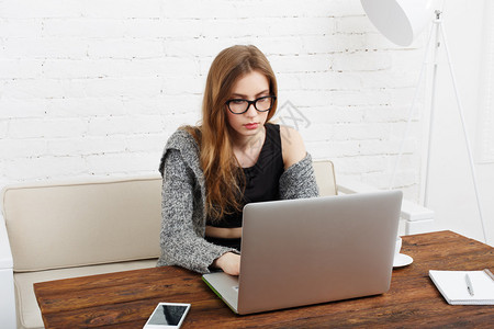 年轻的自由职业者女人坐在她的办公桌前使用笔记本电脑女商人在办公室或在家启动戴眼镜的女人在电脑前工作图片