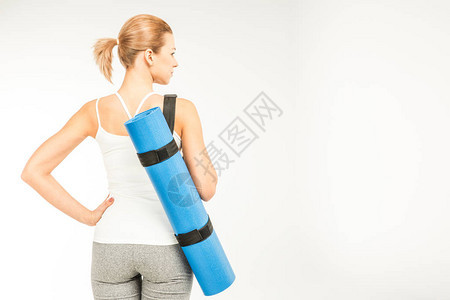 女运动员手持瑜伽垫与白色隔离的背影图片