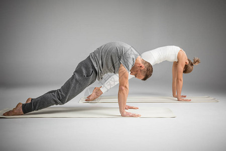 两人一起练习瑜伽在孤立于灰色的瑜伽垫子图片