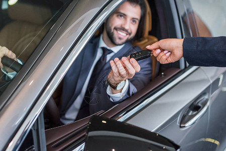 女卖方在经销店将汽车钥匙给予在新车中笑的商图片