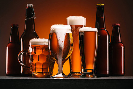 橙色背景下啤酒瓶和大杯的特写视图背景图片