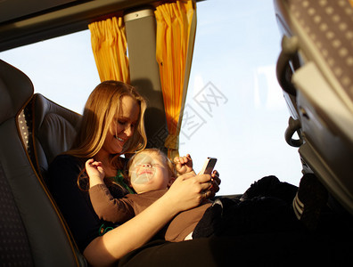 年轻母亲在乘公车旅行时与儿子打电话玩游戏图片