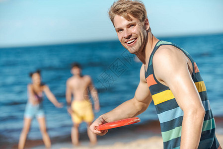 带着飞盘和朋友在沙滩上坐后座的年轻男子微笑图片