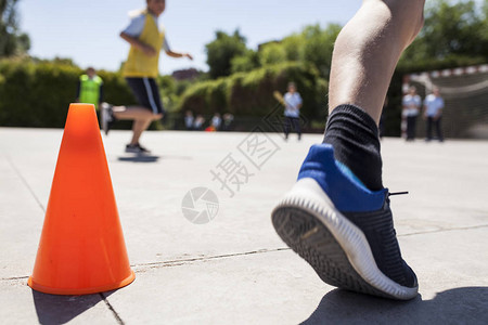 参加体育课跑步的儿童带蓝鞋和橙色锥形的一图片