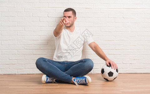 白人年轻男子坐在白砖墙上拿着足球图片