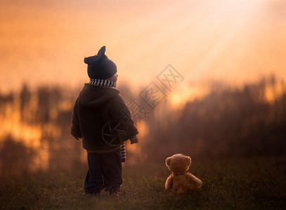 小孩男孩与泰迪熊一起站在湖边的户外图片