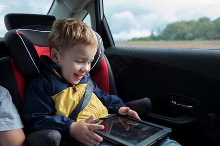 坐在儿童座位和玩平板电脑的车里快乐图片