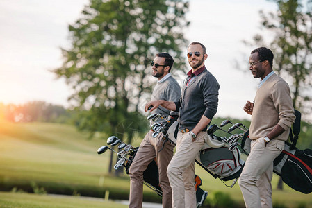 时尚的多民族男子拿着带高尔夫球杆的袋子图片