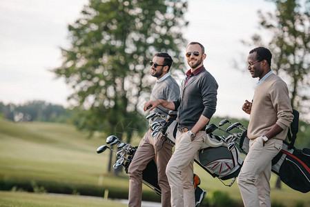 时尚的多民族男子拿着带高尔夫球杆的袋子图片