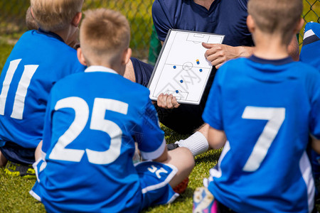 教练儿童足球与教练在体育场的足球队男孩在比赛前听教练的指示教练使用足球战术板图片