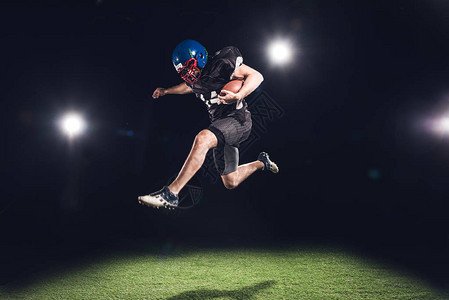 美国足球运动员在黑色聚光灯下与球一图片