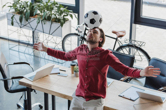 青年商人在办公室头顶上平衡足球的高图片