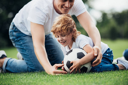 父亲和儿子在公园绿草地上玩足球的快图片