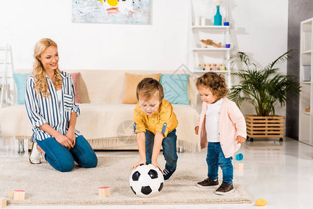 微笑的妈看着可爱的小孩在家里玩足球图片