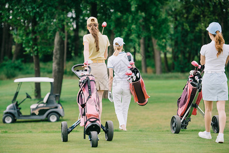 在高尔夫球场的绿色草坪上行走的高尔夫装备女背影图片