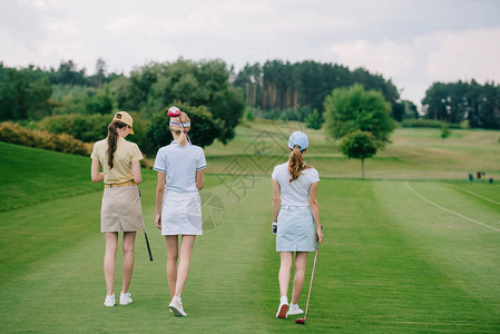 戴着高尔夫设备在高尔夫球场行走的戴帽子的图片