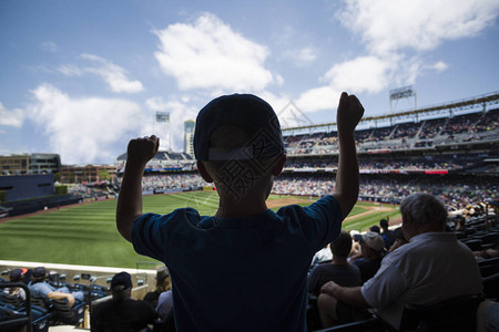 一位兴奋的年轻棒球迷在棒球比赛中在一场激动人心的比赛后站着欢呼男孩兴奋地举图片