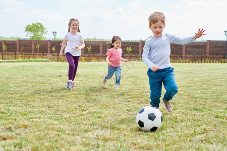 三个快乐的小孩在绿草地前院踢足球图片