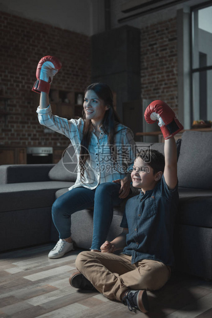 小男孩和他母亲穿着拳击手套在电视上观看比赛图片