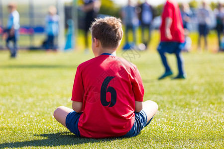 身着运动服的儿童坐在体育场的绿草地上图片