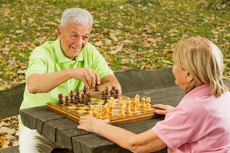快乐的老年夫妇在公园长椅上下棋图片
